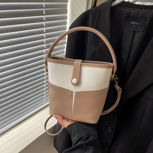 Detail of a two-tone bucket bag featuring beige and cream leather stitching and top handle