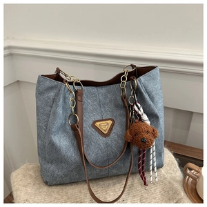 Détail du sac cabas bleu avec bandoulière en cuir brun, chaîne dorée et breloque chien