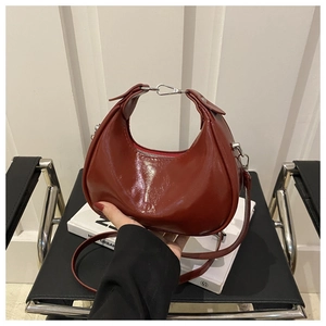 Detail of burgundy patent leather crescent bag with smooth texture and metallic zipper