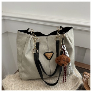 Détail d'un sac cabas en toile avec poignée en cuir noir et breloque ours en peluche