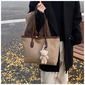 Dettaglio della borsa tote in pelle beige con manici marroni e ciondolo orso