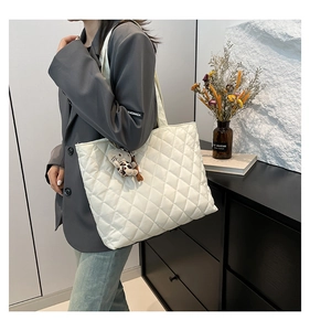 Detailed view of quilted white tote bag with diamond stitching and leopard cat charm