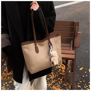 Dettaglio borsa tote con trama litchi, ciondolo a orsetto beige e foulard di seta a quadri