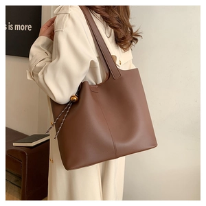 Detail view of deep brown matte leather tote bag featuring drawstring with gold bead accent