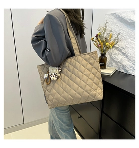 Detail of a khaki quilted tote bag with diamond lattice pattern and cute plush charm pendant