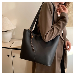 Detail of black faux leather tote with golden ring and woven tassel in lifestyle setting