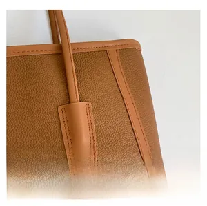 Close-up of brown textured leather tote bag showing fine stitching and strap details