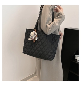 Detail of black quilted tote bag with bear charm shown on a model for lifestyle view