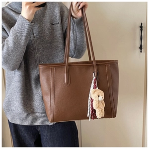 Borsa tote in pelle marrone con ciondolo a forma di orso indossata su maglione grigio