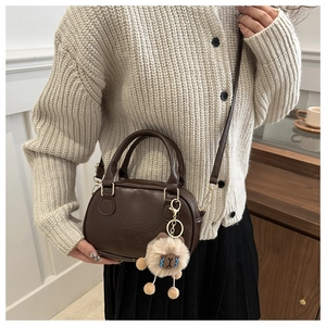 Détail d'un sac bandoulière marron foncé avec lettres embossées et charm en peluche