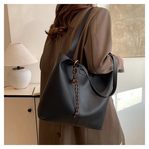 Detail of a large black leather tote bag with woven brown lanyard and metal pendant