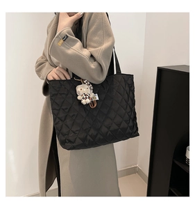 Detail of black quilted oversized tote bag with a cute white cat plush charm on the side