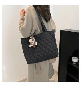 Detail of black quilted tote bag with bear charm shown on model in a minimalist setting