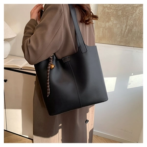 Detail view of large black faux leather tote bag featuring woven rope and bell charm details