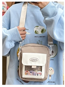 Détail du sac à bandoulière kaki montrant la fenêtre PVC transparente avec des badges