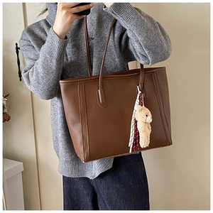 Dettaglio borsa tote in pelle marrone con ciondolo a orsetto e foulard in seta a scacchi