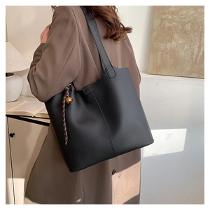 Detail of black matte leather tote bag with gold bell charm worn by a model