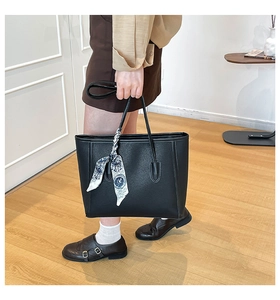 Detail of black pebbled leather tote bag with elegant silk scarf wrap on handle