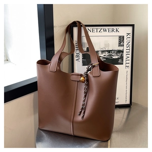 Detail of a dark brown faux leather tote bag featuring a gold bell and woven rope charm