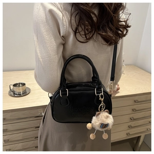 Détail du sac bandoulière noir avec lettrage embossé et adorable breloque ours en peluche