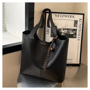 Detailed shot of black matte tote bag with woven charm on a metallic surface