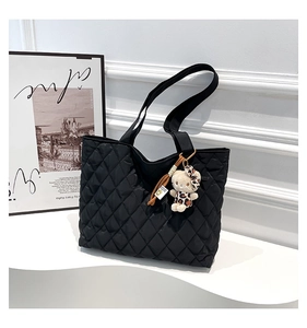 Close-up of black quilted tote bag with wide straps and cute leopard bow bear pendant