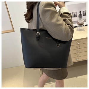 Dettaglio della borsa tote nera con logo dorato indossata su un blazer marrone
