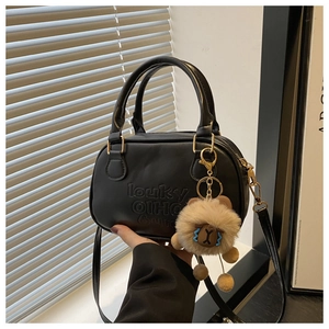 Détail d'un sac à main en cuir noir avec lettres gaufrées et breloque ours en peluche