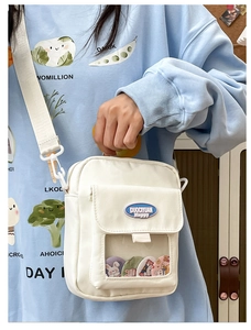 Détail d'un sac à bandoulière en toile blanche avec fenêtre transparente et badges colorés
