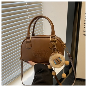 Détail d'un sac Boston marron en cuir avec texte embossé et breloque tête de lion mignonne