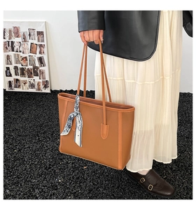 Close-up of caramel brown leather tote bag with silk scarf detail and pebbled texture