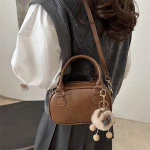 Mini sac Boston en cuir marron rétro avec breloque ours porté par un mannequin chic