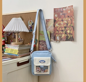 Détail d'un sac bandoulière en toile bleu clair avec poche transparente et badges décoratifs