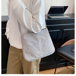 Detailed view of grey corduroy tote bag featuring front pocket on shoulder of a model