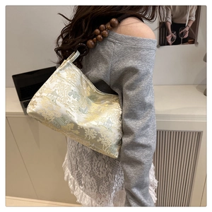 Detail of embroidered silk shoulder bag with wooden bead strap shown on model's shoulder