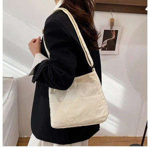Close-up of cream corduroy tote bag texture and shoulder strap on model in black blazer