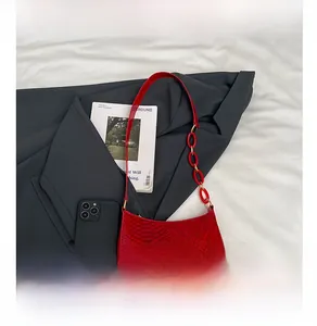 Detail of red snake pattern texture and buckle strap on a shoulder bag next to a phone