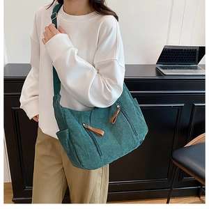 Close-up of dark green corduroy crossbody bag texture and brown leather zipper puller