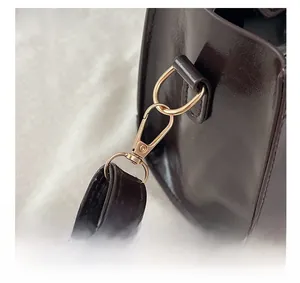 Detailed close-up of light gold lobster clasp and D-ring on dark brown leather handbag