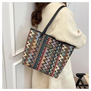 Detail of colorful zigzag knit tote bag with black leather straps on beige wool coat
