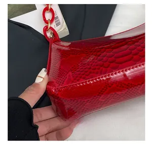Detail shot of a red snakeskin textured handbag featuring bold acrylic chain and stitching