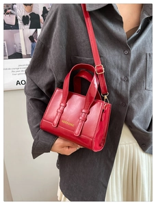 Detailed view of red oil wax leather handbag with FASHION & BAGS lettering and shoulder strap