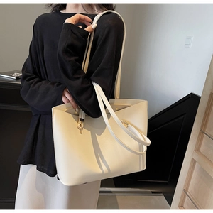 Detail of minimalist cream leather tote bag with long shoulder strap worn by model