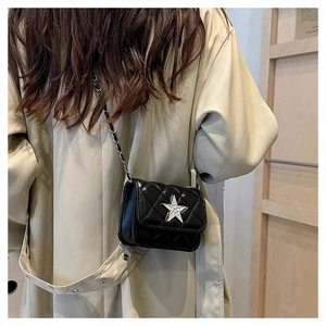 Detail of black quilted crossbody bag with silver star and chain strap on a model