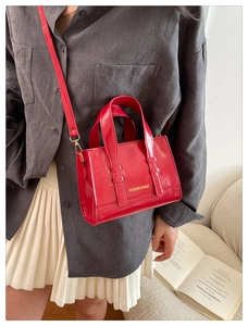 Detail of red oil-wax leather handbag with golden text and detachable shoulder strap