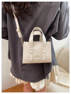 Detail shot of a minimalist creamy white handbag worn by a model in a modern setting