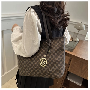 Macro shot of dark brown tote bag with M-pattern logo texture and golden metal pendant