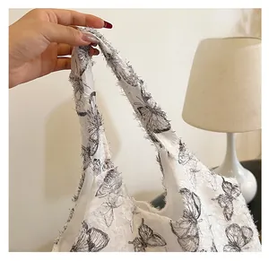 Detail of white tote bag featuring black butterfly prints and frayed tassel edge texture