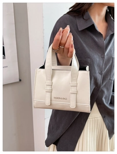 Detail of white faux leather tote bag featuring Fashion & Bags logo and buckle straps