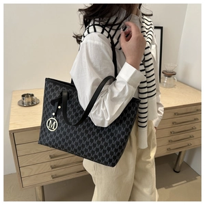 Detailed view of grey monogram tote bag with gold metal M logo charm and black leather handles